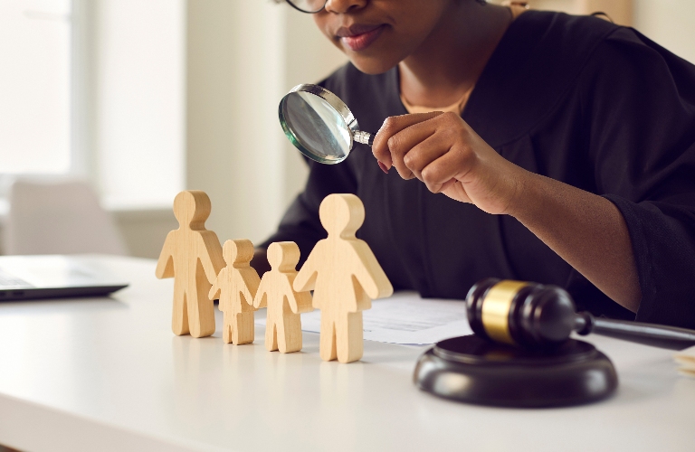 lawyer looking in magnifying glass at little mom, dad children figures on desk